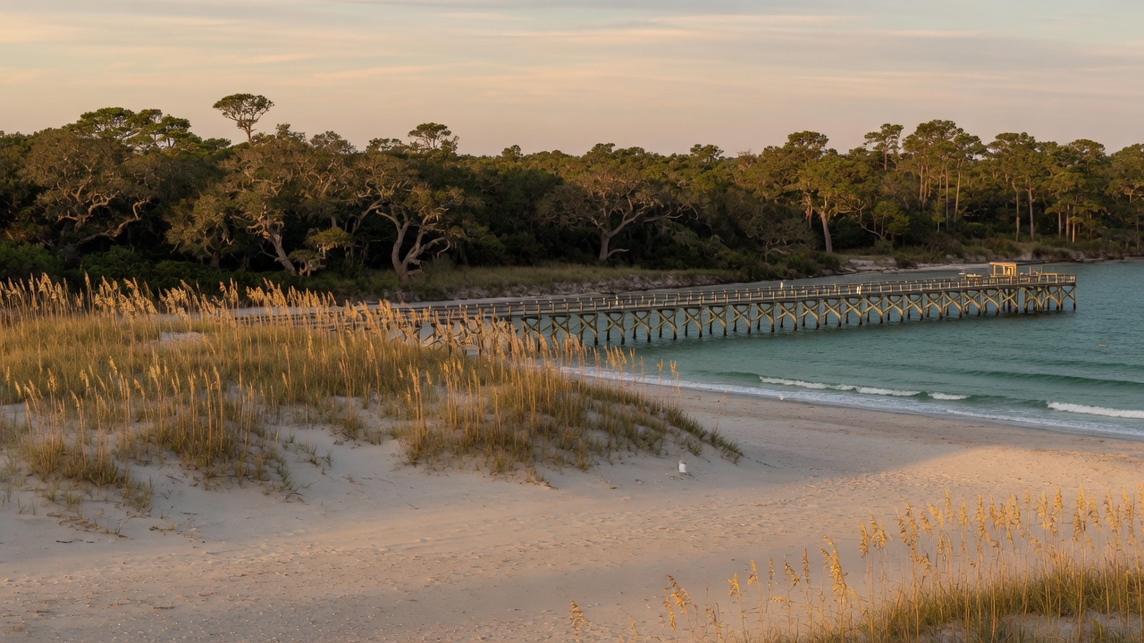 Dunes and sea oats on a pale-sand Topsail Island beach, with a wooden fishing pier and teal Atlantic water at late afternoon